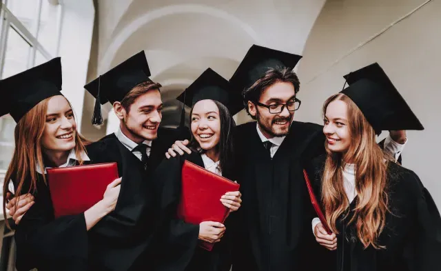 Five college graduates holding diplomas celebrating on graduation day